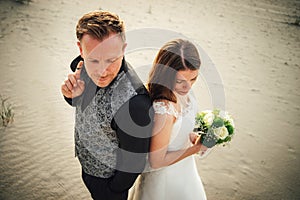 Closeup view on bride and groom standing on sandy beach and looking the same direction. Attractive newlyweds in evening