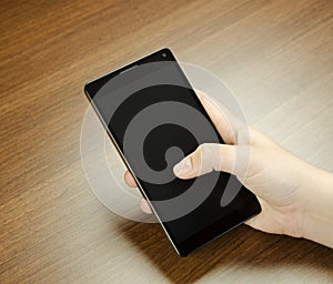 Closeup view of a child hand with fingers holding a black cell phone with black screen on wooden mat blur