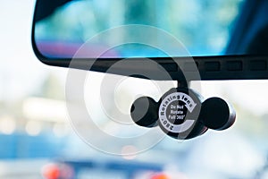 Closeup view of a DVR camera attached to a rearview mirror in a car against a blurred background. A device designed to record