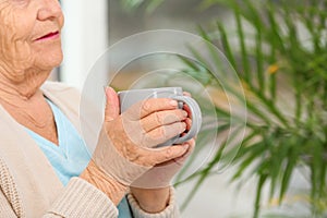 Closeup view of elderly woman with cup of tea in nursing home, space for text. Assisting