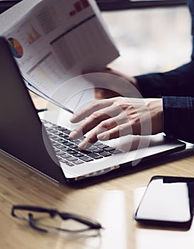 Closeup view of Elegant businessman working at sunny office on laptop computer while sitting at the wooden table.Man