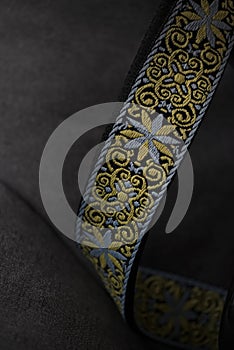Embroidered guitar strap with decorative yellow and blue pattern on dark fabric surface in soft studio lighting