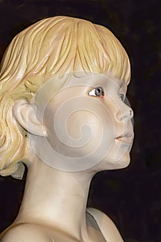Closeup view of face of old retro mannequin girl with short blond hair and a chip in her nose and a spider behind her ear against