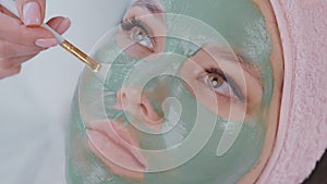 closeup view of female face in beauty salon, aesthetician applying clay mask on skin
