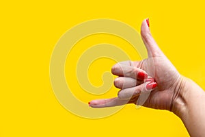 Closeup view of female hand forming gesture call me. Isolated on bright yellow background.