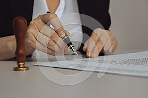 Closeup view of female hand holding pen. Paper and stamp on the desk.
