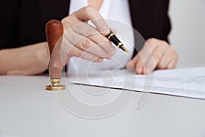 Closeup view of female hand holding pen. Paper and stamp on the desk.