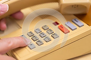 Closeup view of finger dialing telephone number on old style wired desktop telephone - studio shot