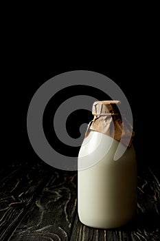 closeup view of fresh milk in bottle wrapped by paper on black background