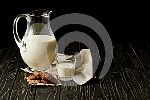 closeup view of fresh milk in jug and glass, chocolate cookies and sackcloth on black background