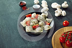 Closeup view on fresh ravioli with slice cherry tomato on black plate and dark background.