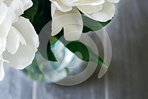 Closeup view of a glass vase with lush white peony petals against a blurred gray background. Beautiful flower as a gift