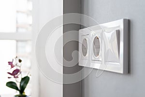 A closeup view of a group of white european electrical outlets and a switch located on a gray wall in a light modern kitchen