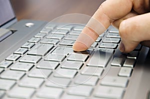 Closeup view of a hand with a finger press the Enter key on the silver keyboard laptop lying on a wooden mat