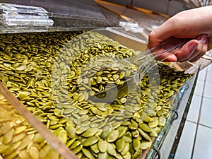 Closeup view of a hand picking up some pumpkin seeds with a plastic spoon in a shop store as a healthy snack