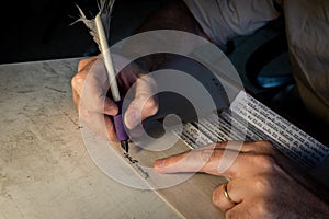 Closeup view of the hands of a Jewish scribe writing the words of the Shema Yisrael prayer on parchment that will be encased in a photo