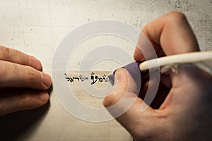 Closeup view of the hands of a Jewish scribe writing the words of the Shema Yisrael prayer on parchment that will be encased in a photo