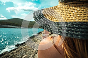 Closeup view of a hay hat, unrecognizable brunette seen from behind. Amazing blue adriatic sea blurred in the distance, concepts