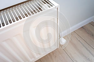 Closeup view of a home heating radiator in a living room with wooden floor and light wall