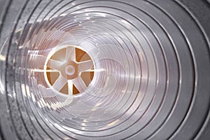 Closeup view from inside the galvanized steel air duct on the exhaust fan in the background light, the front and back background