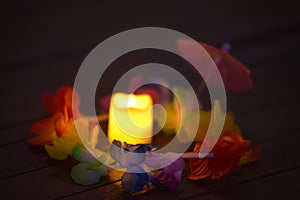 Closeup view of lighting candle between beautiful artificial colorful flowers