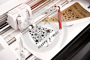 closeup view on machine head of plotting machine that cuts christmas sticker with lettering from black adhesive vinyl.