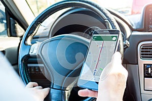 Closeup view of male hands with a mobile phone with map on screen while driving a car. Using the navigator on smartphone