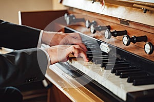 Closeup view on male hands in suit playing at pipe organ in church. Vintage classic musical instrument.