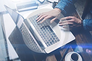 Closeup view of male hands typing laptop keyboard.Modern notebook, cup of black coffee and smartphone on the wooden