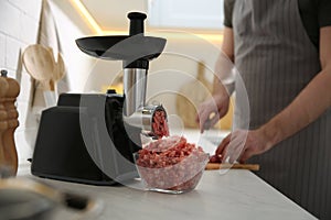 Closeup view of man cutting ingredients in kitchen, focus on meat grinder