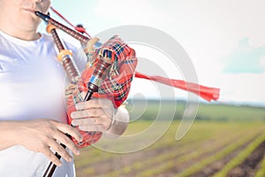 Closeup view of man enjoying playing pipes in traditional style. Green outdoors summer field background