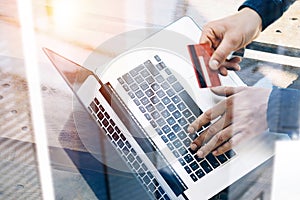 Closeup view of Man holding credit card in hand and typing laptop keyboard while sitting at the wooden table.Reflections