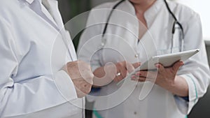 Closeup view of man and woman doctors using tablet during working day at clinic. Caucasian person and his female