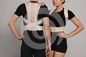Closeup view of man and woman with orthopedic corsets on grey background