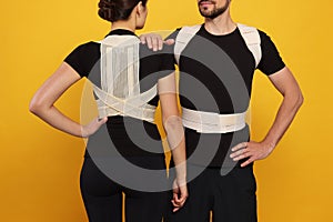 Closeup view of man and woman with orthopedic corsets on orange background