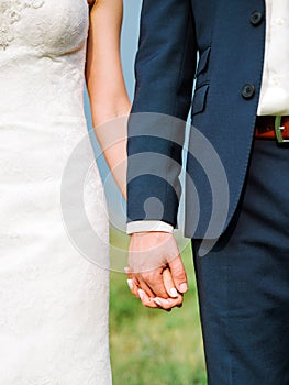 Closeup view of married couple holding hands. Summer wedding concept. Outdoor wedding ceremony.
