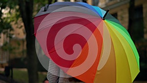 Closeup view of an open spinning colourful rainbow umbrella in female hands. Slowmotion shot