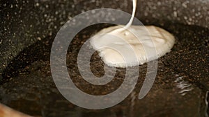 Closeup view pouring fresh white pancake dough mixture into preheat cast iron pan with vegetable oil at home