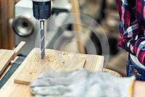 Closeup view professional carpenter hand making hole with electric drill in wood plank in carpentry diy workshop. Detail of