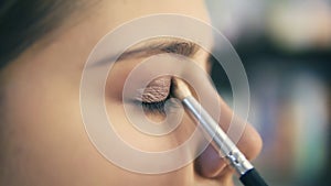 Closeup view of professional makeup artist hands using makeup brush to apply eye shadows. Pro visagiste puts light brown