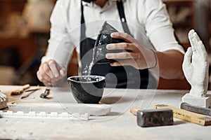 Unrecognizable professional stonemason with well-maintained hands making glue in special vessel for his handmade photo