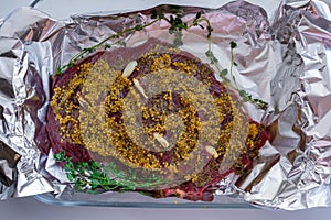 Closeup view of a raw slab of beef meat stuffed with garlic slices and covered in wholegrain mustard and spices