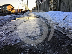 A closeup view of slippery black ice covering a sidewalk in the early morning of a residential neighbourhood during the winter