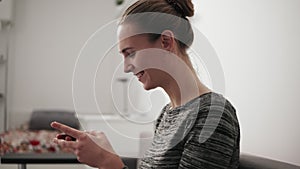 Closeup view of a smiling young woman sitting on the couch at home looking at phone and typing a message