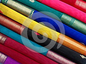 Closeup view of stacked saris or sarees in display of retail shop, for use as indian textiles background