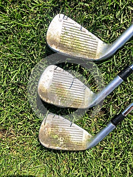 A closeup view of three golf irons with dirty grooves that need cleaning