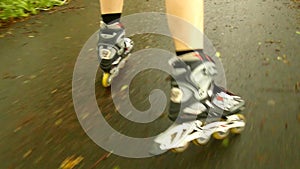 A closeup view to legs in white rollerblades. The man is quickly blading on asphalt way in park