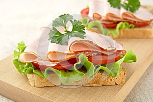 Closeup view of toasts,lettuce,tomato,cold cuts on cutting board