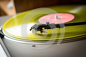 Closeup view of a tonearm and turntable playing color yellow vinyl record