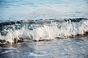 Closeup view of transparent sea water wave over the pebbles and sand
